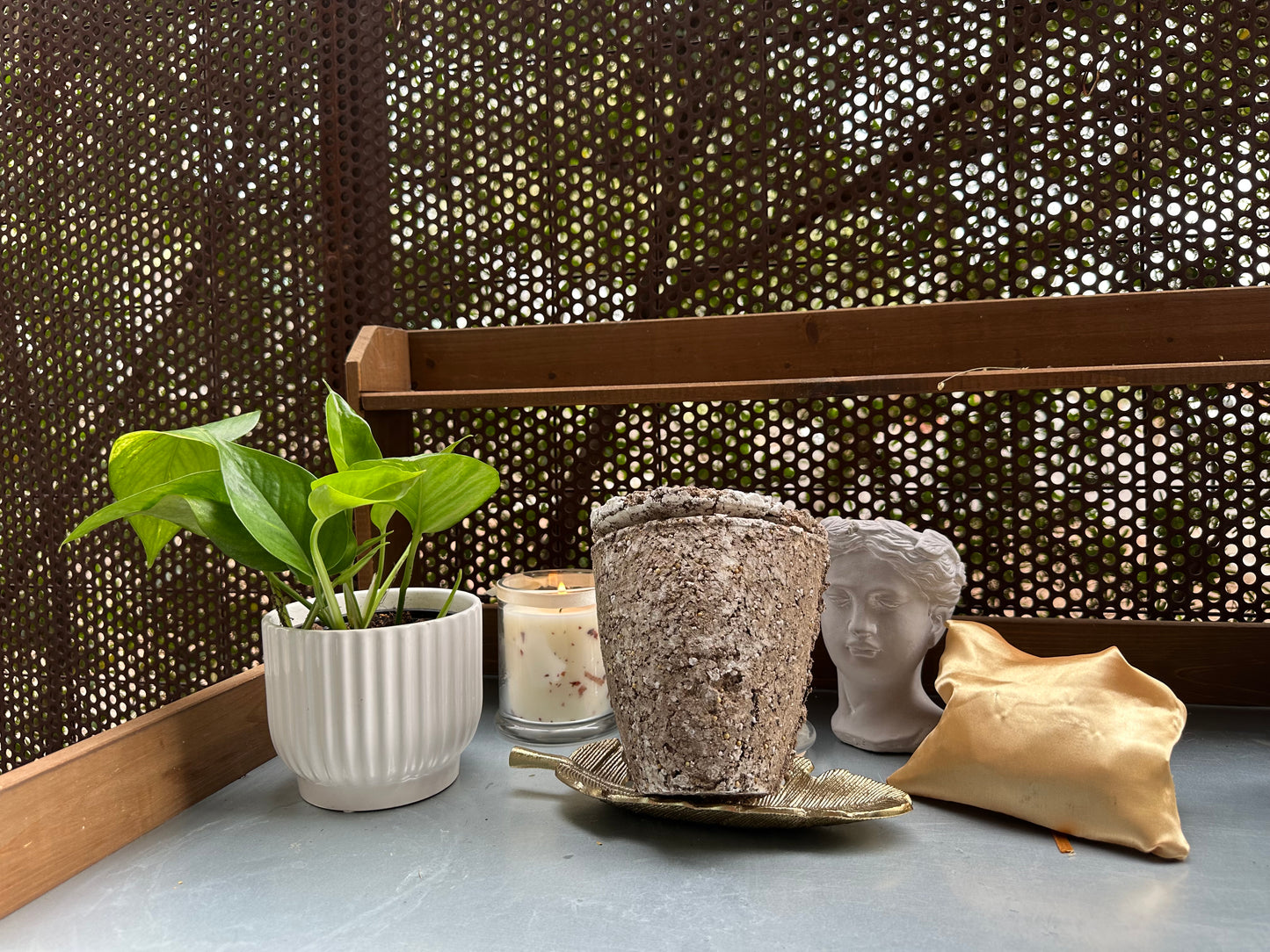 Decorative items including a potted plant, candles, and decorative heads on a surface with a textured wall background. and an Afterleaf Eco Urn.