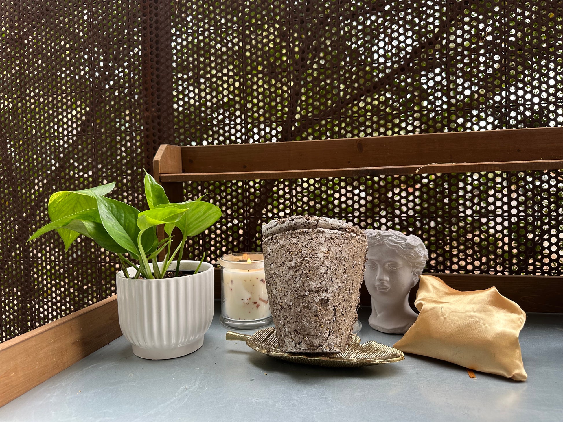 Decorative items including a potted plant, candles, and decorative heads on a surface with a textured wall background. and an Afterleaf Eco Urn.